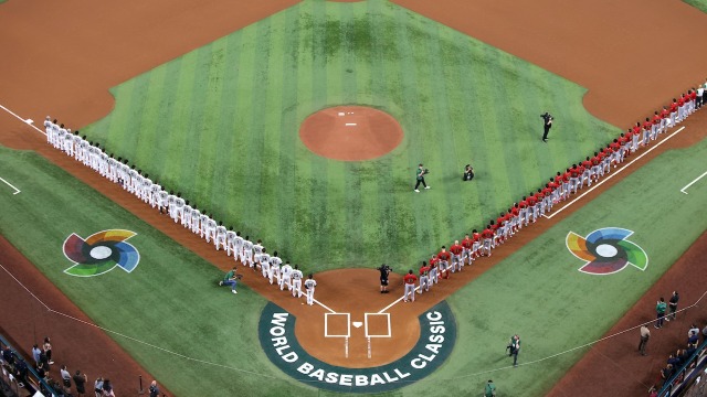 alt="2 teams lined up on either side of the World Baseball Classic baseball diamond during national anthem"