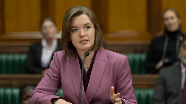 alt="Amy James-Kelly as Jennifer Bevan speaking at a hearing, wearing a pink blazer"