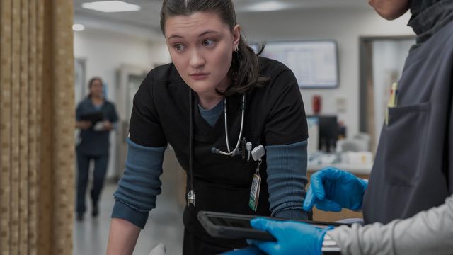 alt="Dr. Trinity Santos leans over a patient bed, reviewing information"