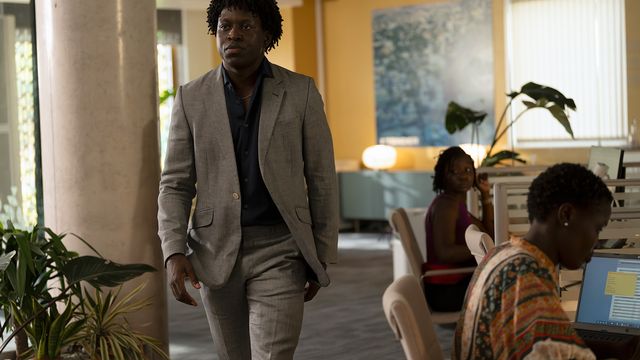 alt="Kwabena Bannerman walks through an office wearing a gray suit"